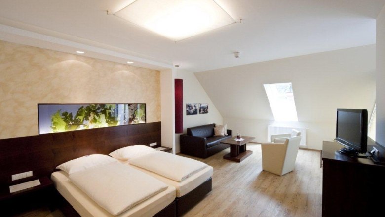 Modern eingerichtetes Hotelzimmer mit Doppelbett, Sofa, Sessel und Fernseher.