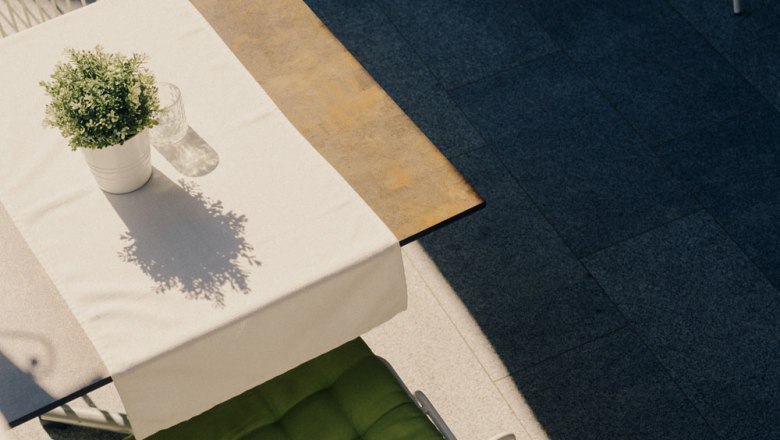 Ein Tisch mit weißer Tischdecke, Topfpflanze und Glas im Freien.