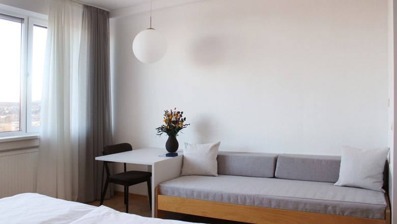 Modernes G&auml;stezimmer mit Sofa, Tisch, Stuhl und Fenster mit Vorh&auml;ngen.