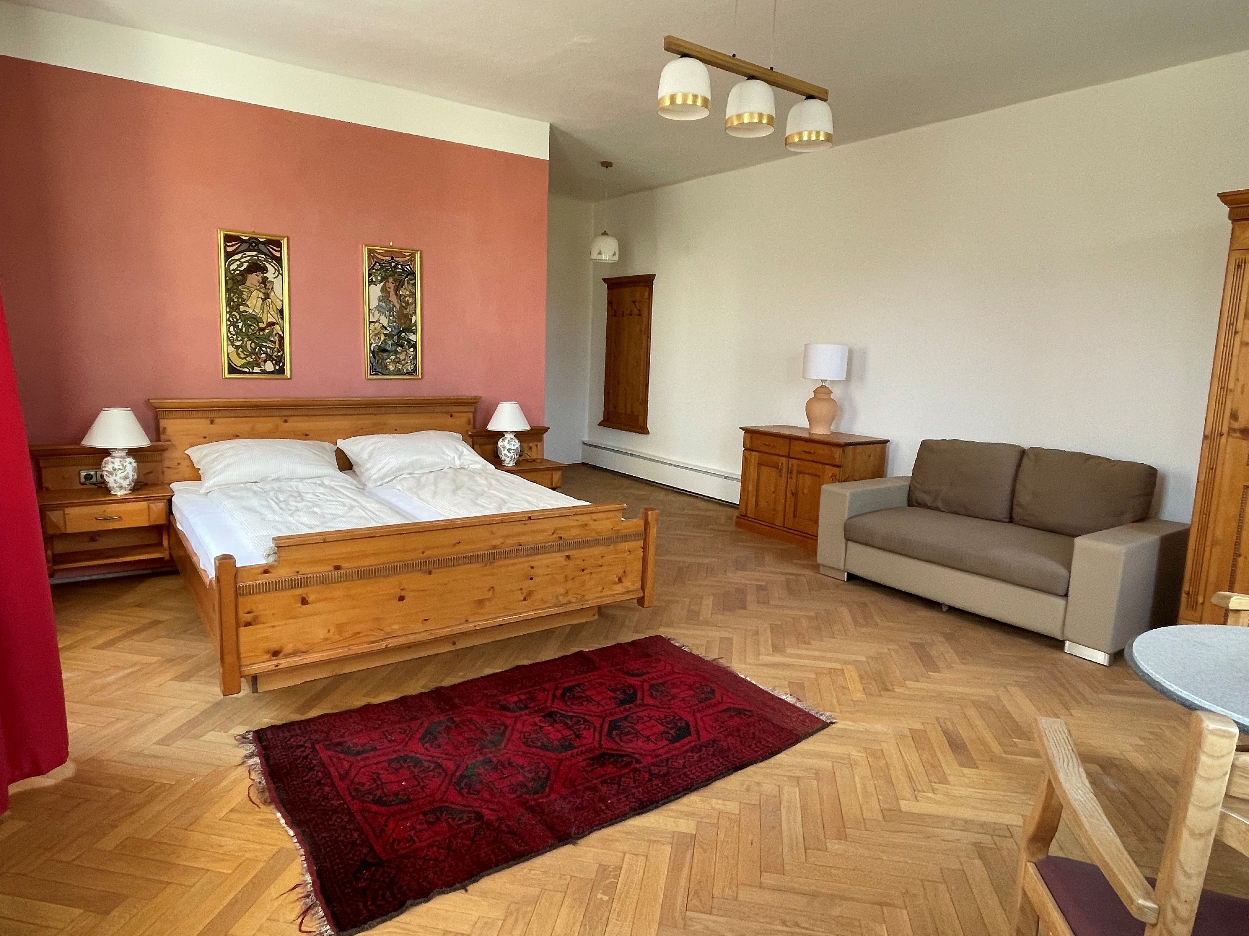 Ein geräumiges Schlafzimmer mit einem Holzbett, Nachttischen, einer Couch und einem roten Teppich auf Holzboden.