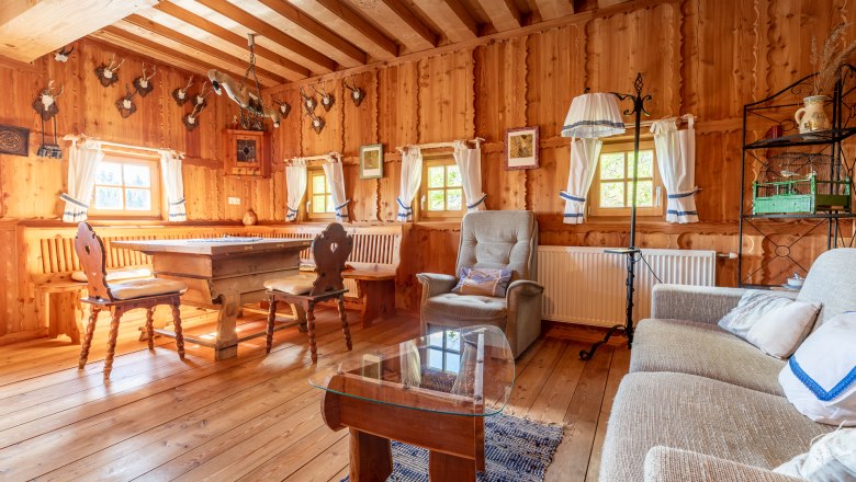 Rustikaler Wohn- und Essbereich mit Holzm&ouml;beln, Holzw&auml;nden und Jagdtroph&auml;en an der Wand.