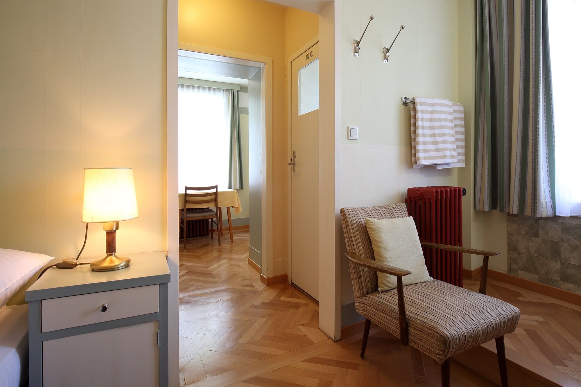 Innenansicht eines Zimmers im Looshaus mit Sessel, Nachttischlampe und Tisch im Hintergrund.