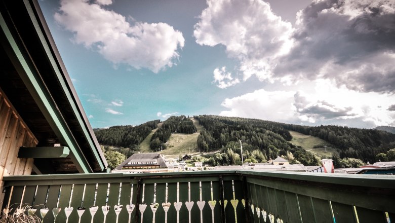 Blick von einem Balkon auf eine grüne Berglandschaft mit Wolken am Himmel.