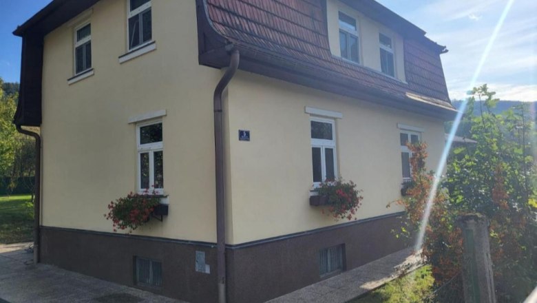 Zweistöckiges gelbes Haus mit roten Dachziegeln und Blumenkästen an den Fenstern.