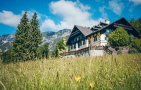 Ein traditionelles Geb&auml;ude namens Knappenhof in einer gr&uuml;nen Wiese vor einer Bergkulisse.