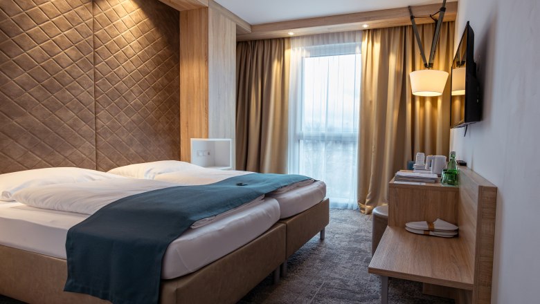 Das Alfred, © Niederösterreich Werbung / Maximilian Pawlikowsky Modernes Hotelzimmer mit Doppelbett, Holzverkleidung und Fenster mit Vorhängen.