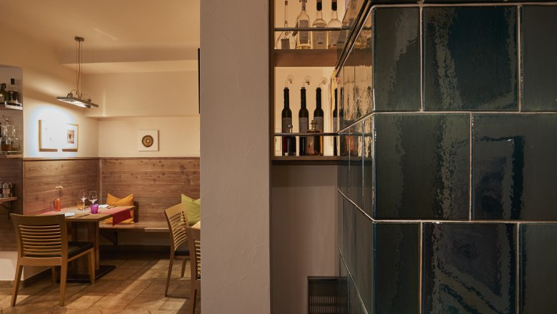 Gem&uuml;tliche Stube mit Holzm&ouml;beln, Kachelofen und Flaschenregal.