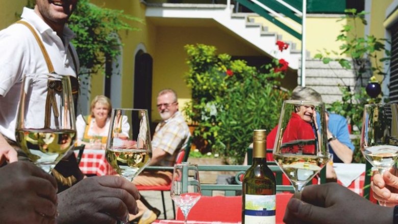 Menschen stoßen mit Weingläsern im sonnigen Innenhof an.