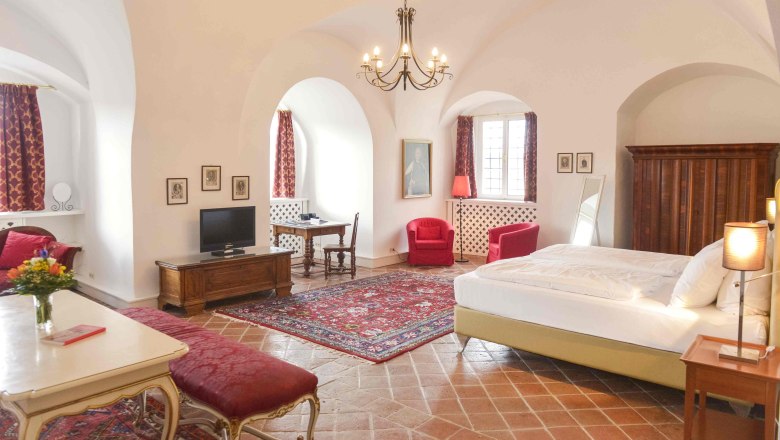 Luxuriöse Suite mit antiken Möbeln, roten Teppichen und Vorhängen, einem großen Bett und einem Kronleuchter.