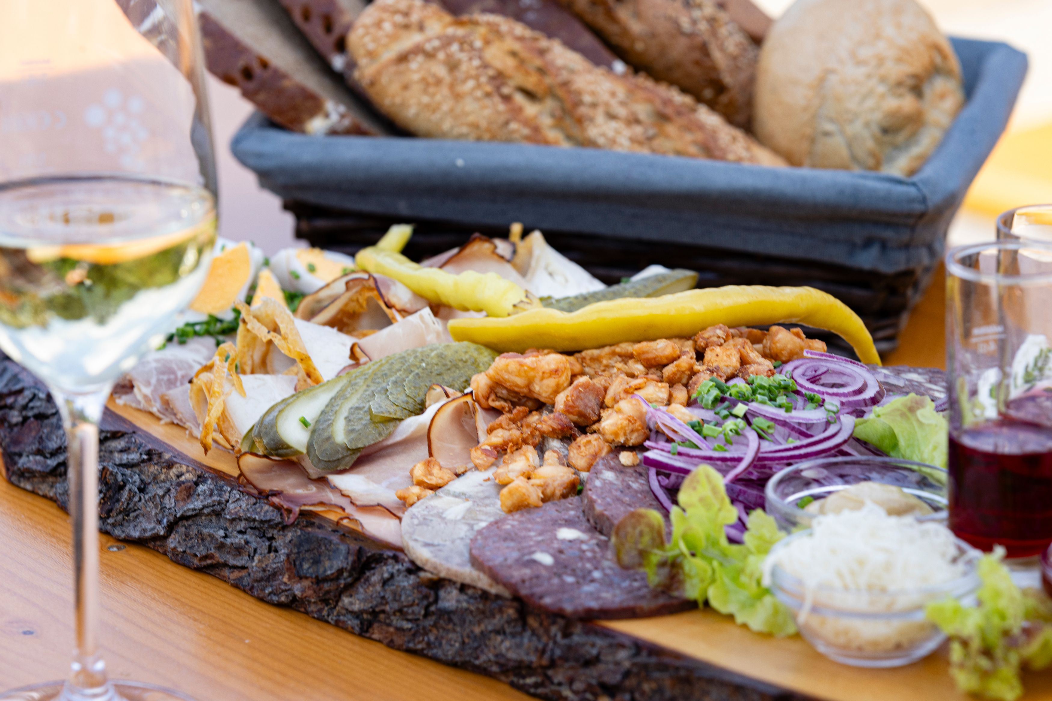 Heurigenplatte mit Wurst, Käse, Zwiebeln und Brot auf einem Holztisch.