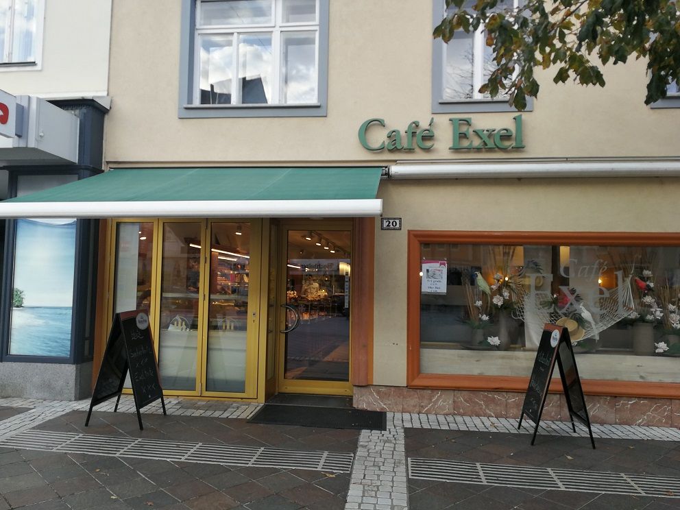 Außenansicht des Café Exel mit grüner Markise und Schaufensterdekoration.