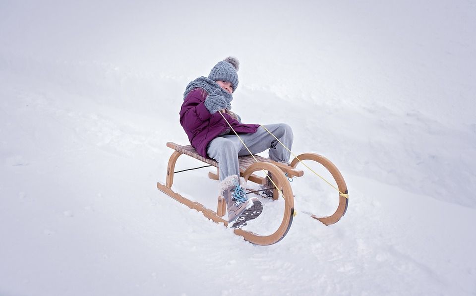 Kind in Winterkleidung sitzt auf einem Holzschlitten im Schnee.