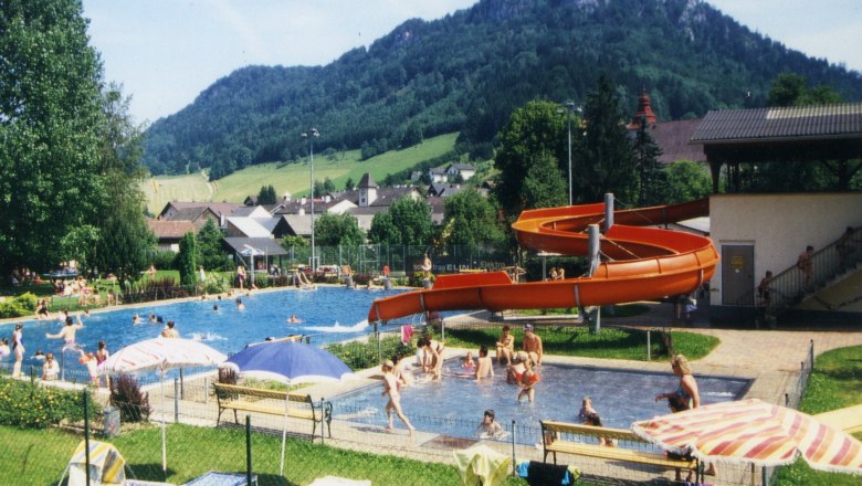 Freibad mit Rutsche und Berglandschaft im Hintergrund.