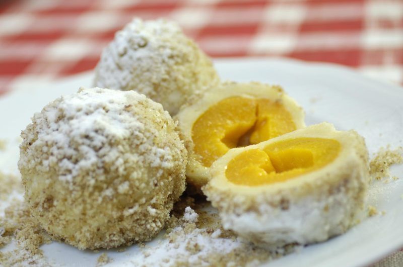 Drei Marillenknödel auf einem Teller, einer davon aufgeschnitten