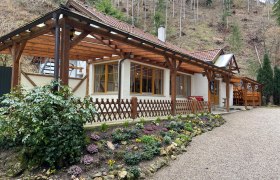 Ein Gasthaus mit Holzdach und Blumengarten vor einem bewaldeten Hang.