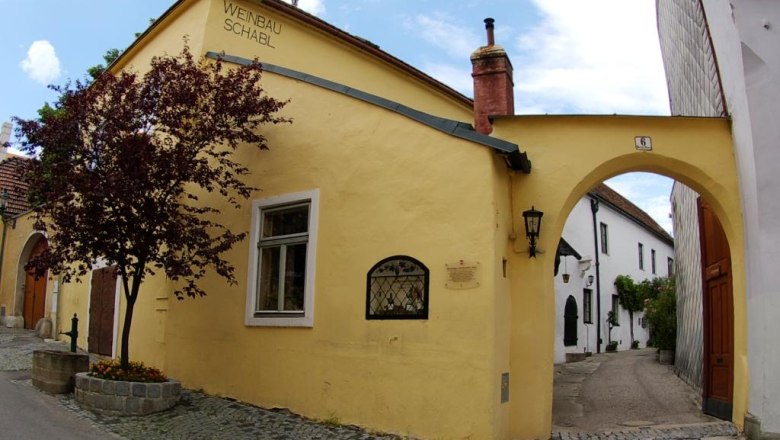 Gelbes Geb&auml;ude mit der Aufschrift 'Weinbau Schabl', daneben ein Torbogen und ein Baum.