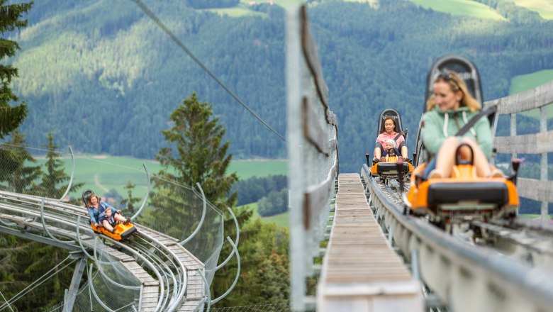 Menschen fahren auf einer Sommerrodelbahn in den Bergen.