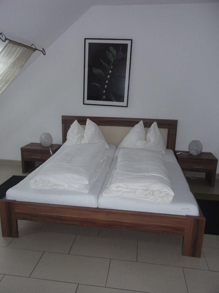 Doppelbett in einem Hotelzimmer mit weißer Bettwäsche und einem Pflanzenbild an der Wand.