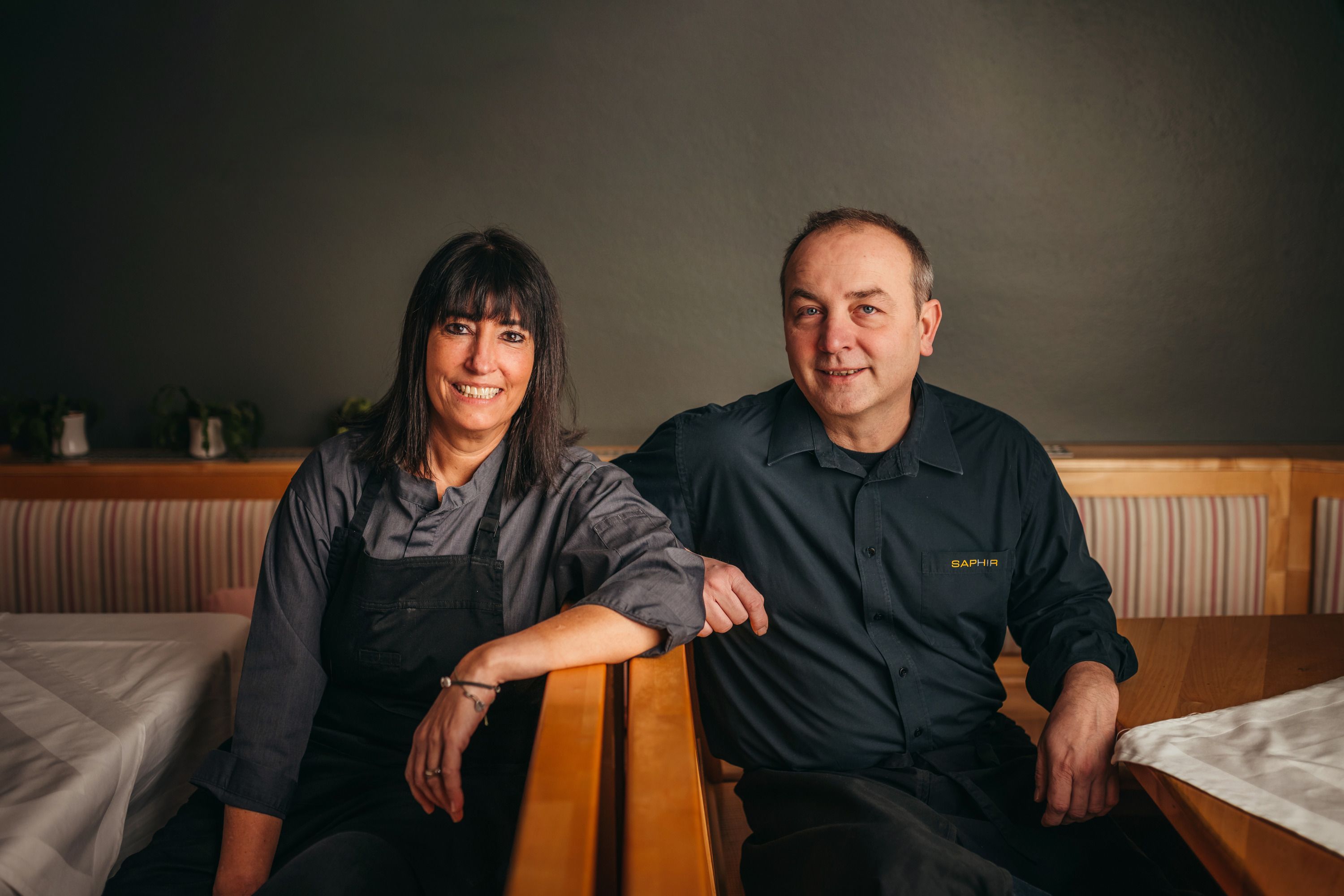 Zwei Personen in Arbeitskleidung sitzen lächelnd in einem Restaurant.