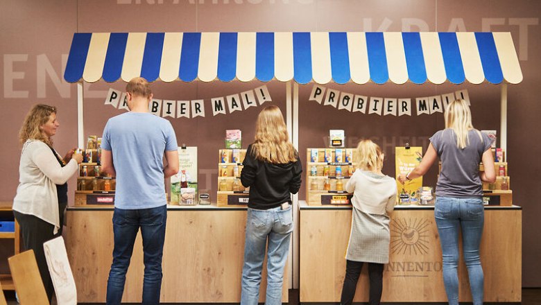 Menschen probieren Produkte an einem Stand mit blau-wei&szlig;em Dach.