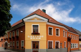 Ein traditionelles Gasthaus mit orange-gelber Fassade und roten Dachziegeln unter blauem Himmel.