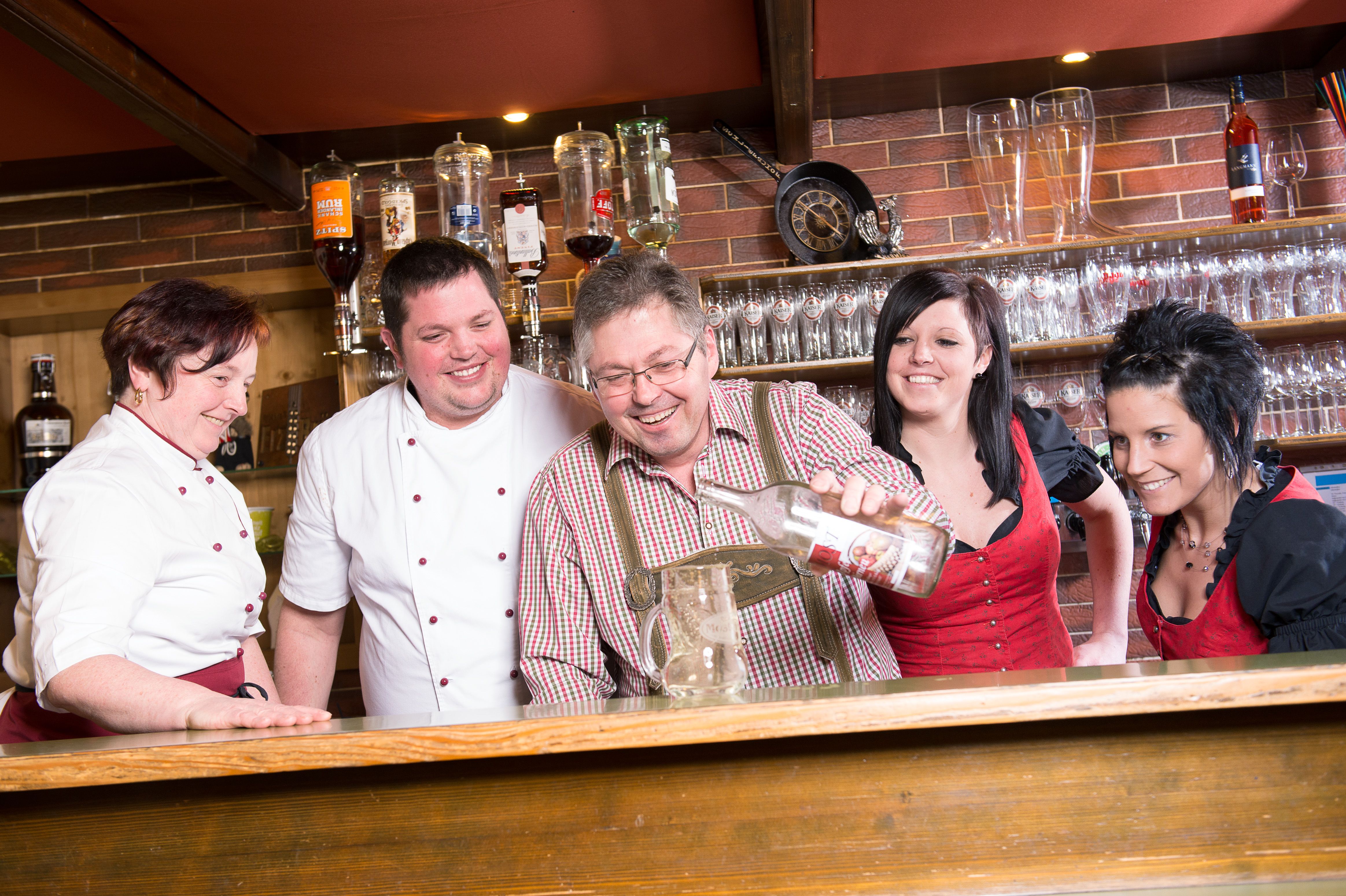 Eine Gruppe von Menschen hinter einer Bar, die gemeinsam lachen und eine Flasche in einen Krug gießen.
