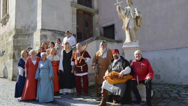 Gruppe von Menschen in mittelalterlicher Kleidung vor einer Statue in einer Altstadt.