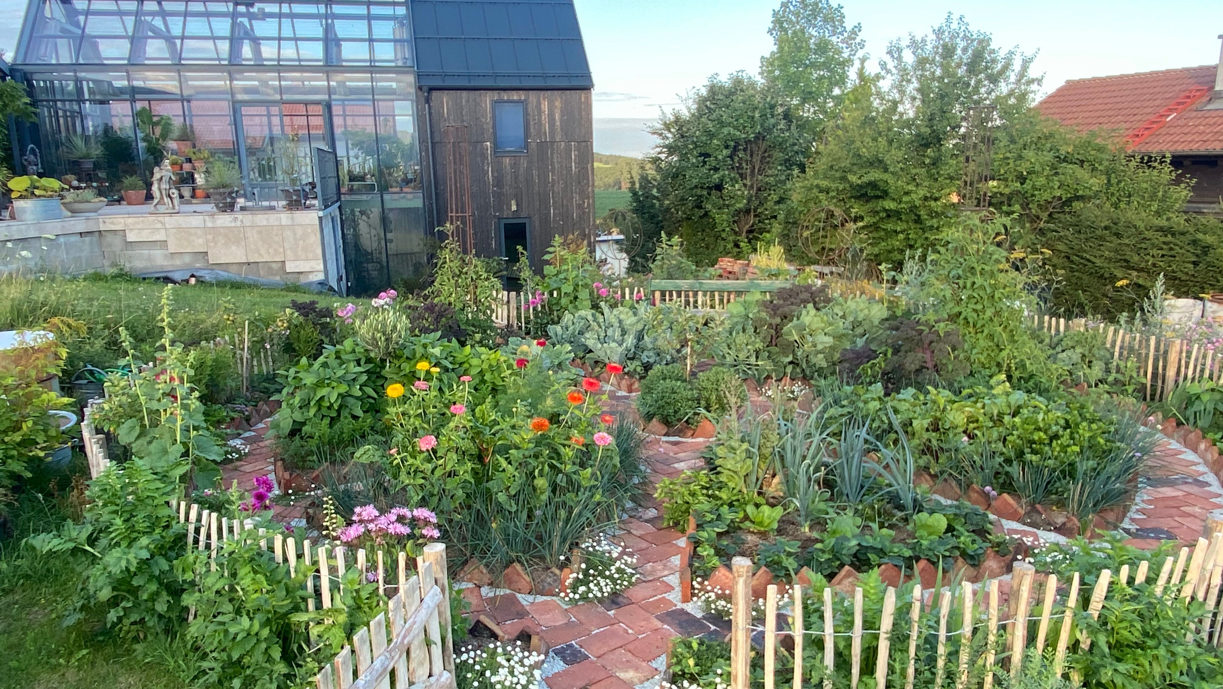 Ein Glashaus von außen im Ecolution.Lab mit einem bunten Garten im Vordergrund.