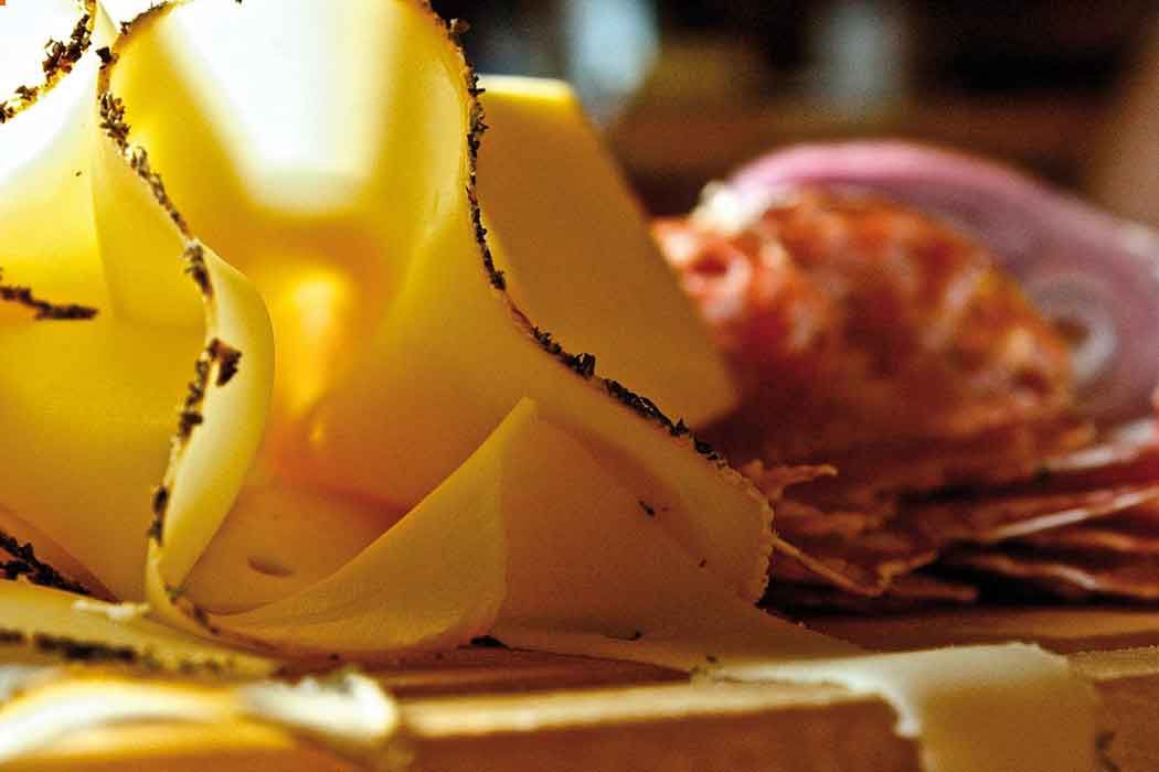 Nahaufnahme von dünn geschnittenem Käse und Wurst auf einem Holzbrett.