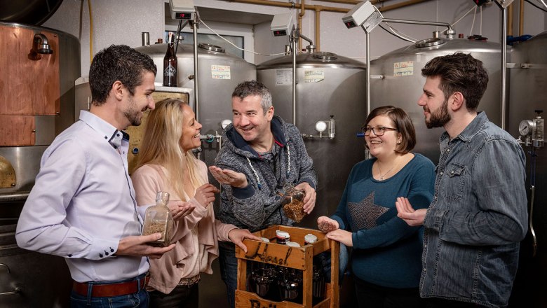 Gruppe von Menschen in einer Brauerei mit Bierflaschen und Zutaten.
