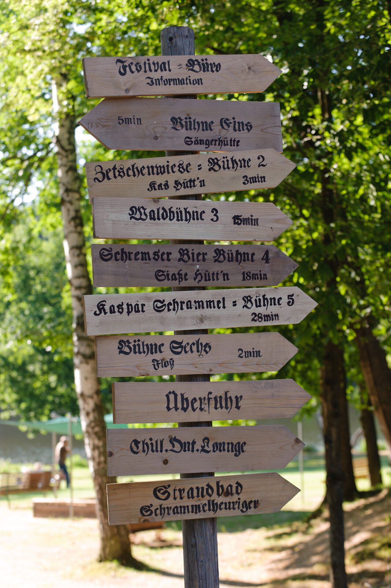 Ein malerischer Wegweiser steht umgeben von üppigem Grün und strahlendem Sonnenlicht. Die verschiedenen Richtungen laden dazu ein, die Schönheit der Natur zu erkunden und die vielfältigen Angebote des Festivals zu entdecken. Hier, wo Musik und Natur harmonisch verschmelzen, wird jeder Schritt zu einem unvergesslichen Erlebnis.