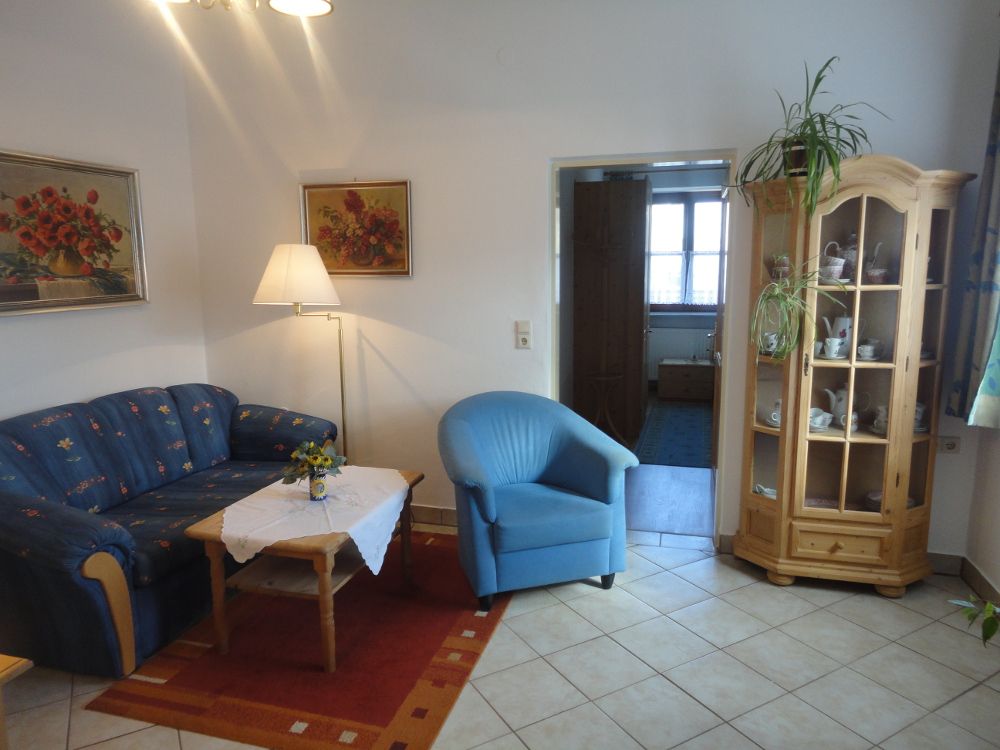 Wohnzimmer mit blauer Couch, blauem Sessel, Holztisch und Vitrine.