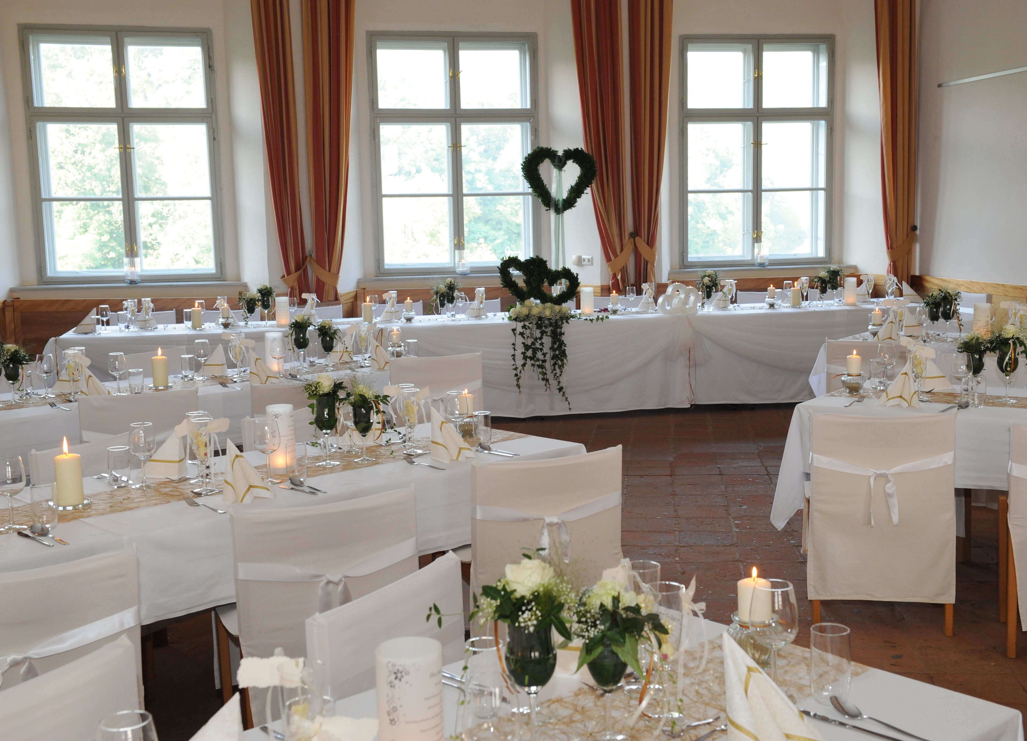 Eleganter Festsaal mit gedeckten Tischen, weißen Stuhlhussen und Kerzen.
