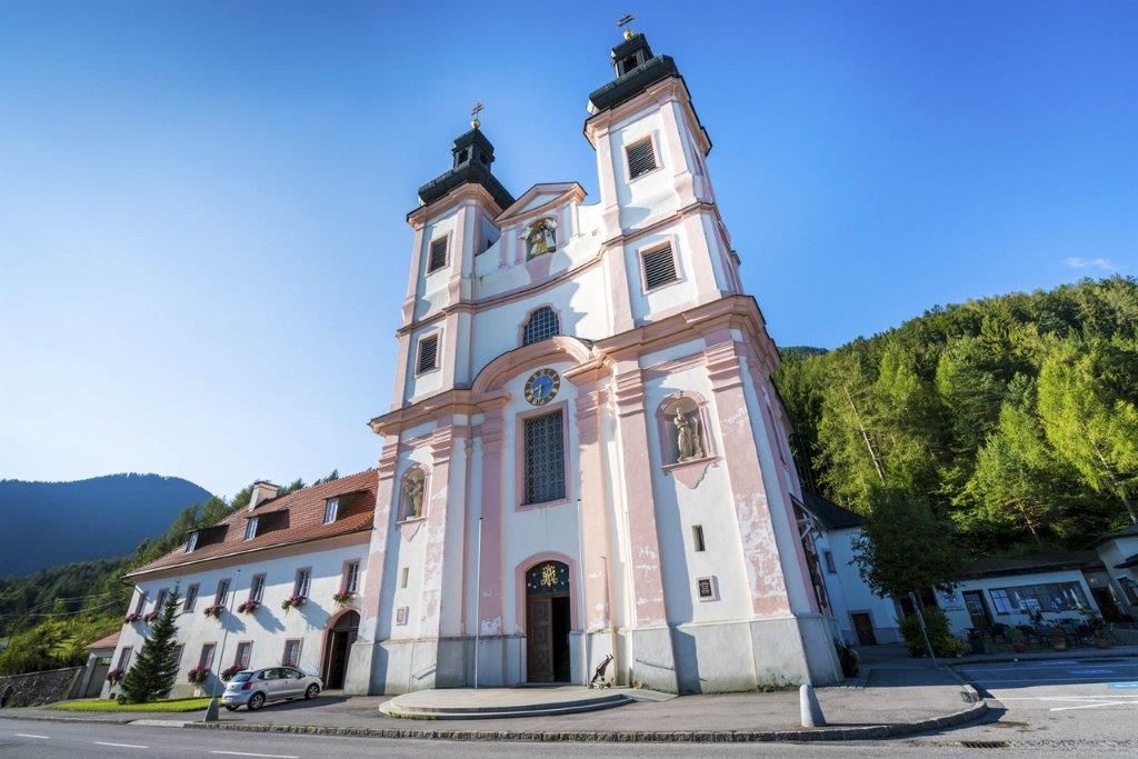 Wallfahrtskirche Maria Schutz mit blauem Himmel und grünen Bäumen im Hintergrund.