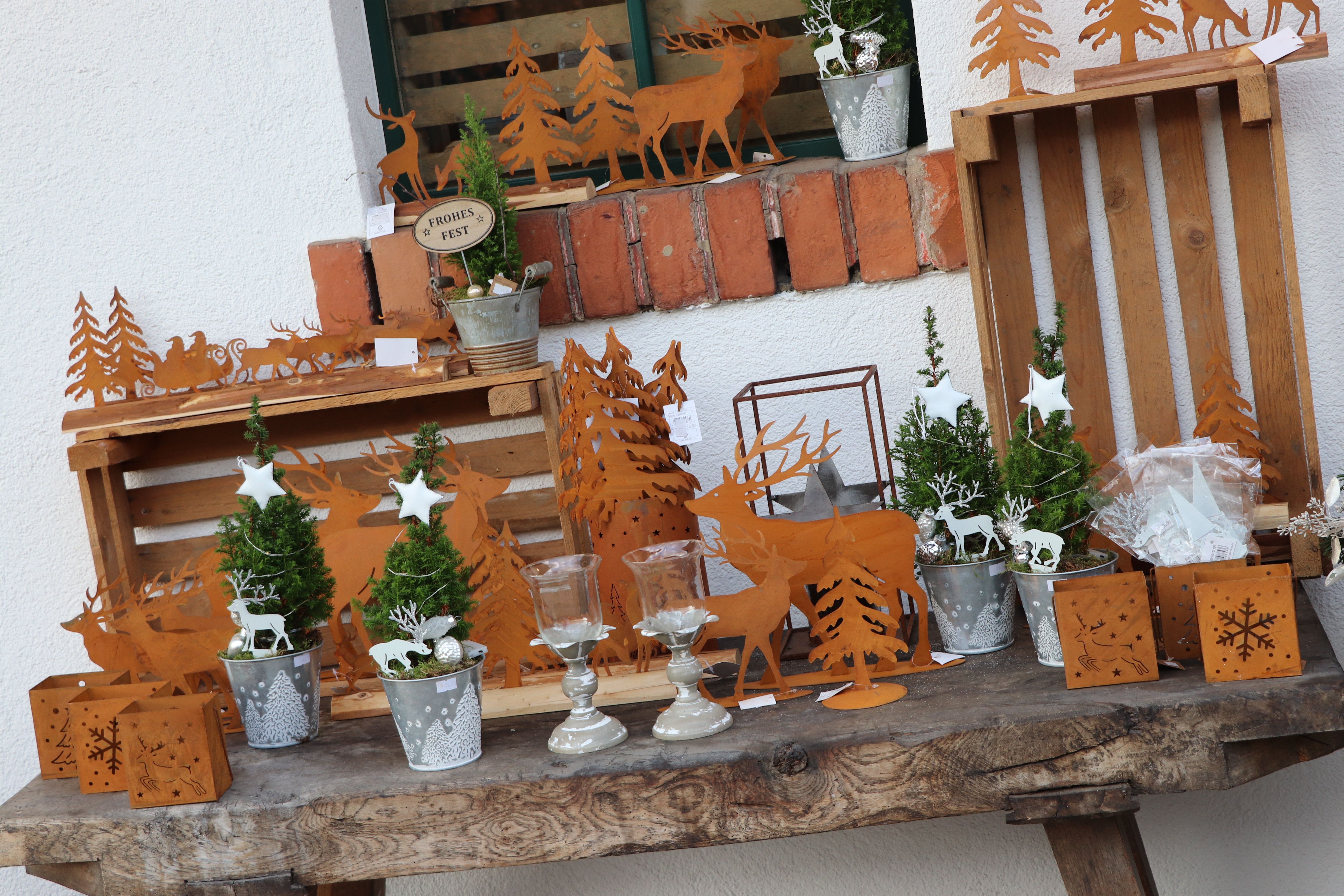 Weihnachtliche Dekoration mit Rentier- und Tannenbaum-Motiven aus Metall auf einem Holztisch.