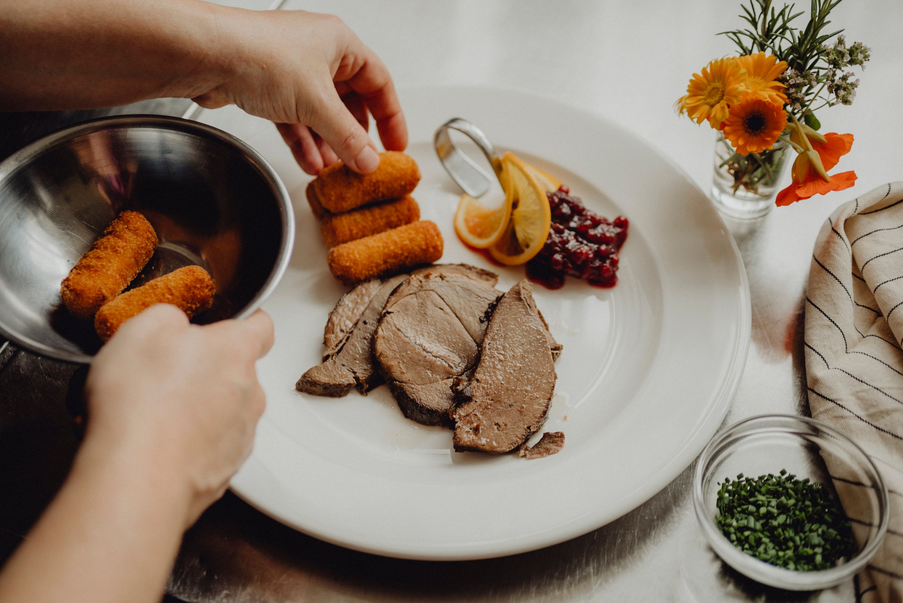 Ein Teller mit Fleisch, Kroketten, Preiselbeeren und Zitronenscheiben wird angerichtet.