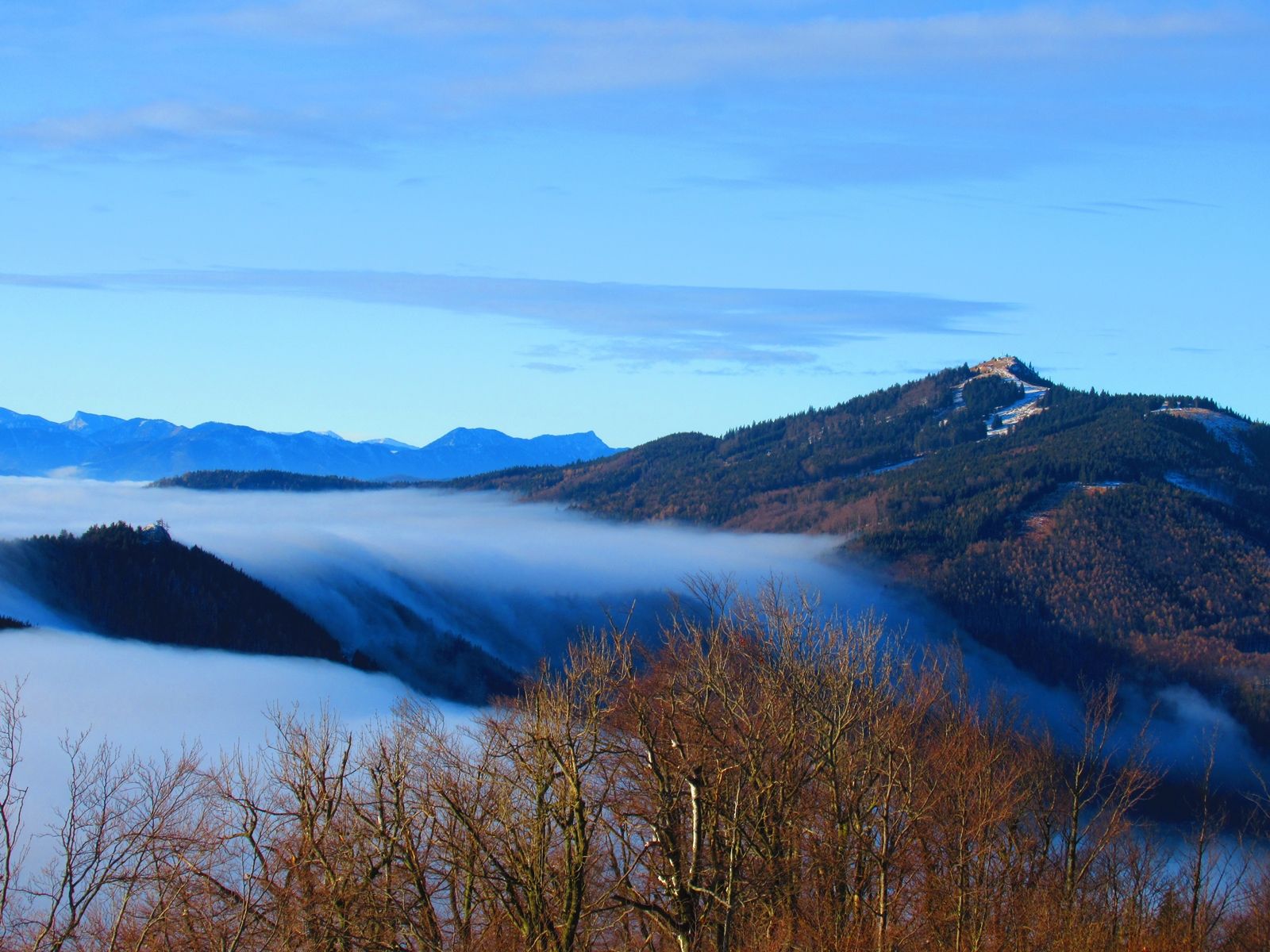 Blick von einem Berg auf nebelverhangene Täler und bewaldete Hügel.
