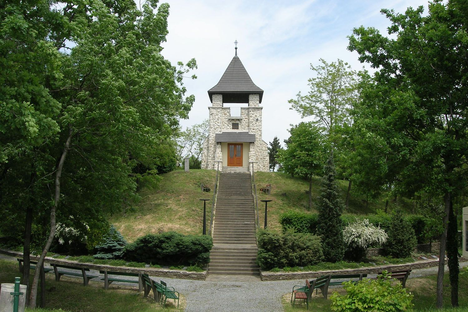 Ein steinernes Kriegerdenkmal mit Turm und Treppe, umgeben von Bäumen und Bänken.