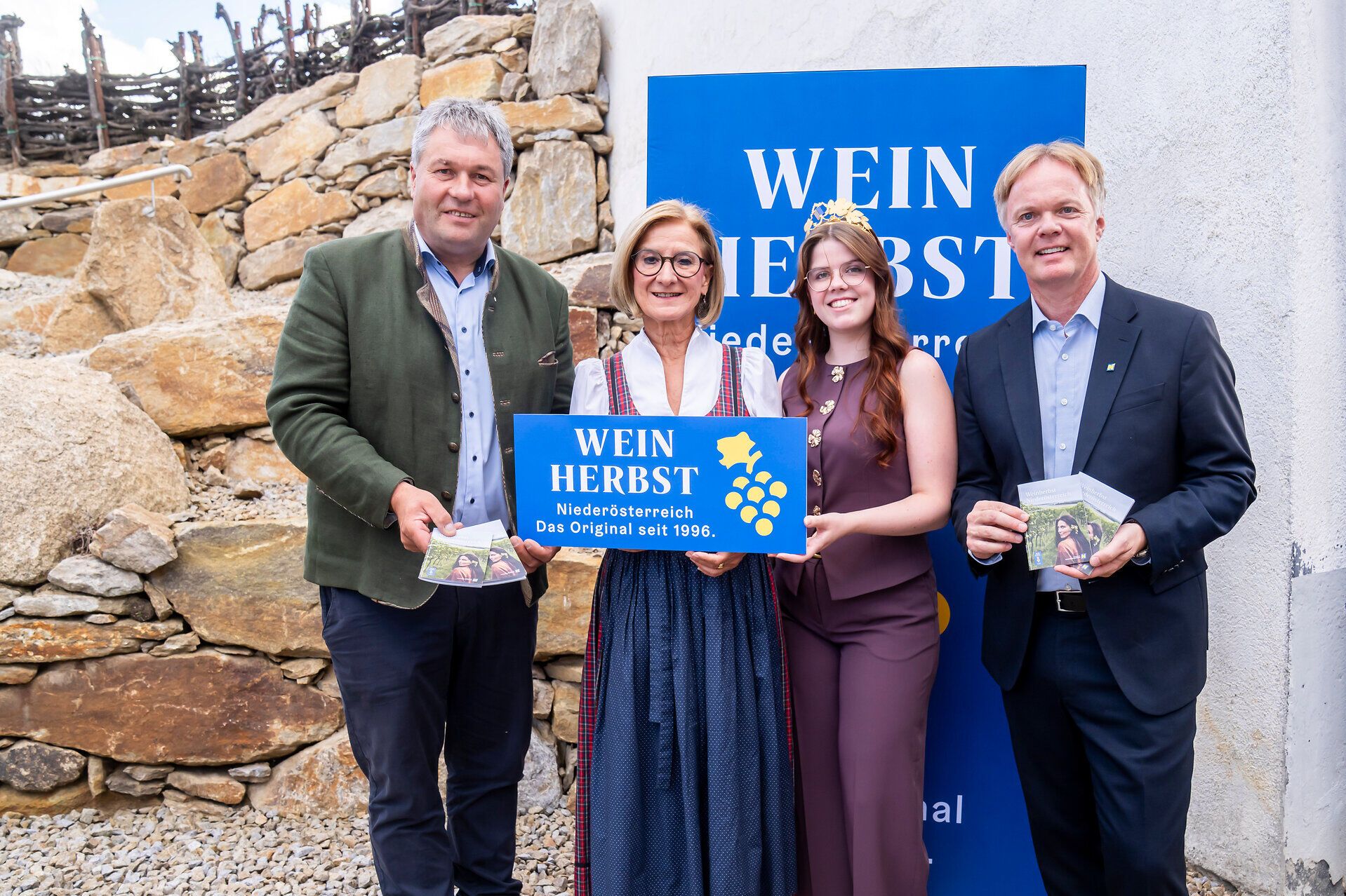 Vier Personen stehen vor einem Weinherbst-Niederösterreich-Aufsteller und präsentieren gemeinsam das Weinherbst-Schild sowie die aktuelle Weinherbst-Broschüre.