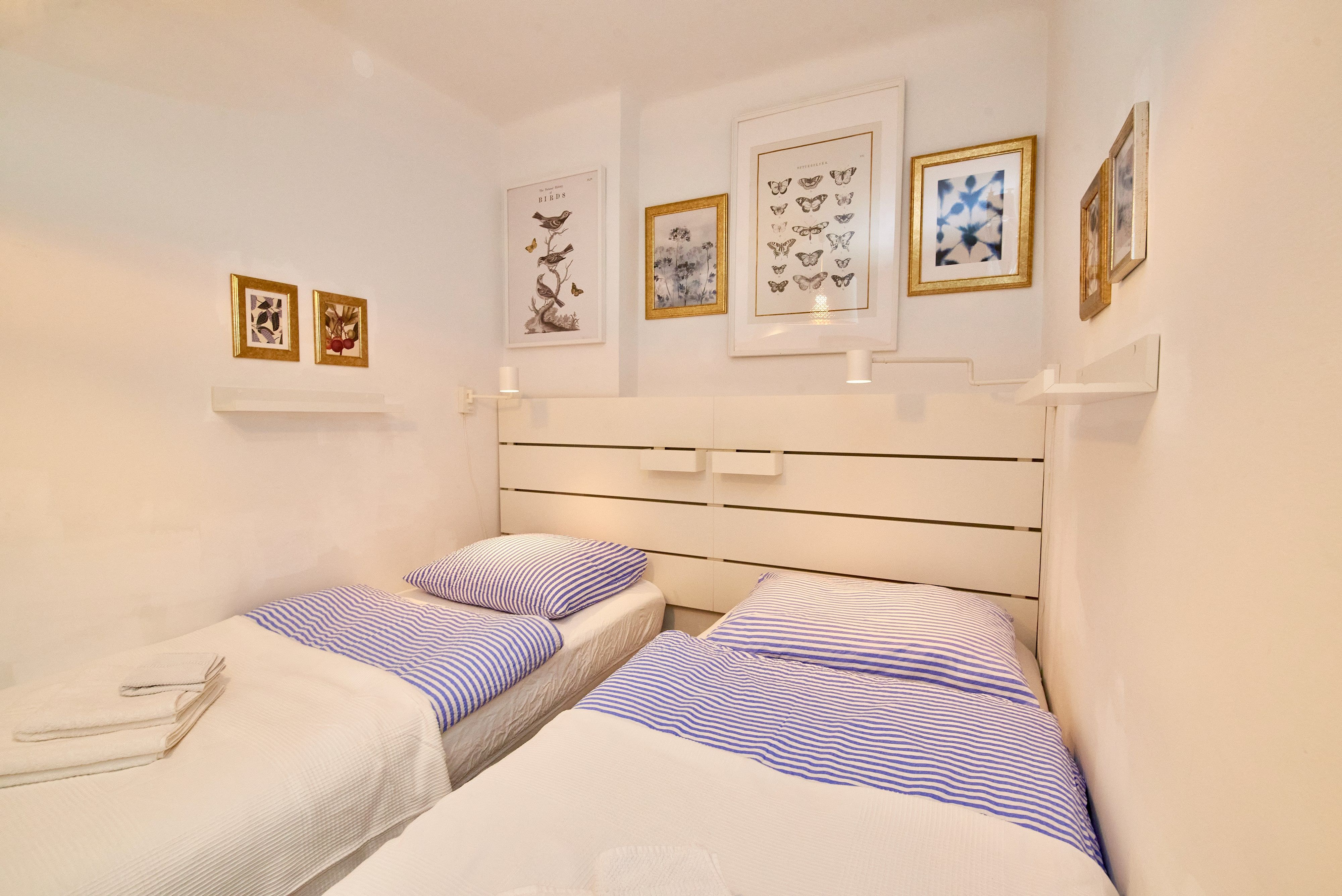Zwei Einzelbetten mit blauen Streifenbettwäsche in einem hellen Schlafzimmer mit dekorativen Bildern an der Wand.