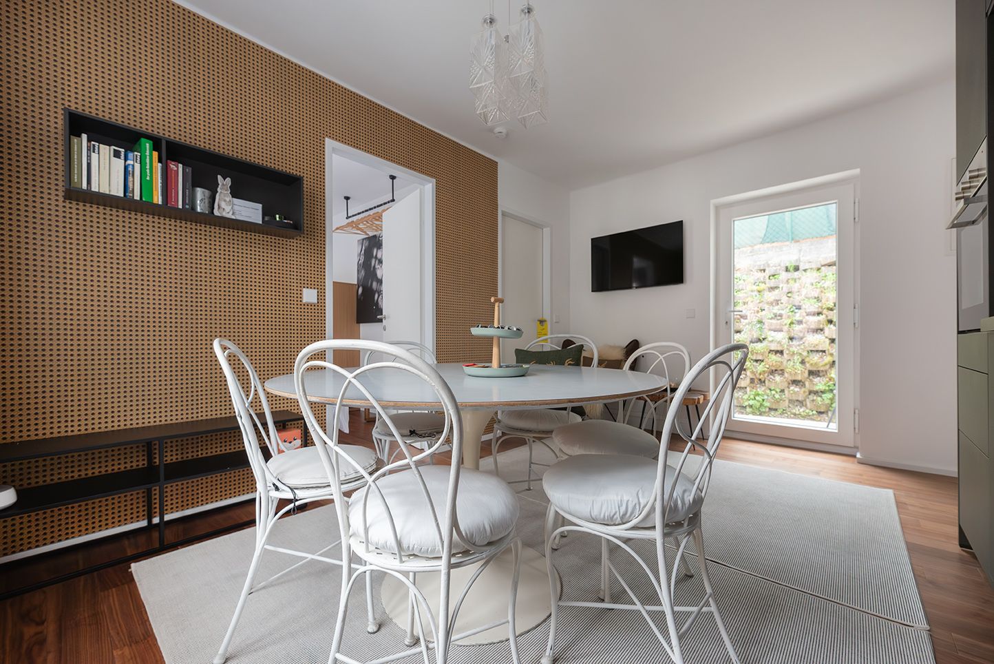 Esszimmer mit rundem Tisch und weißen Stühlen, Holzwand und Bücherregal.