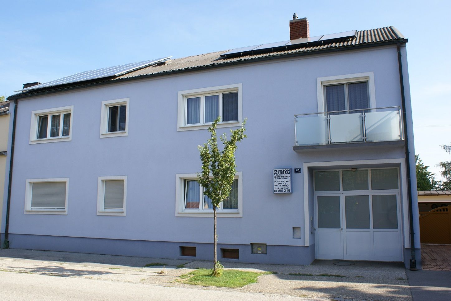 Außenansicht eines zweistöckigen Gebäudes mit blauer Fassade und Solarpanels auf dem Dach.