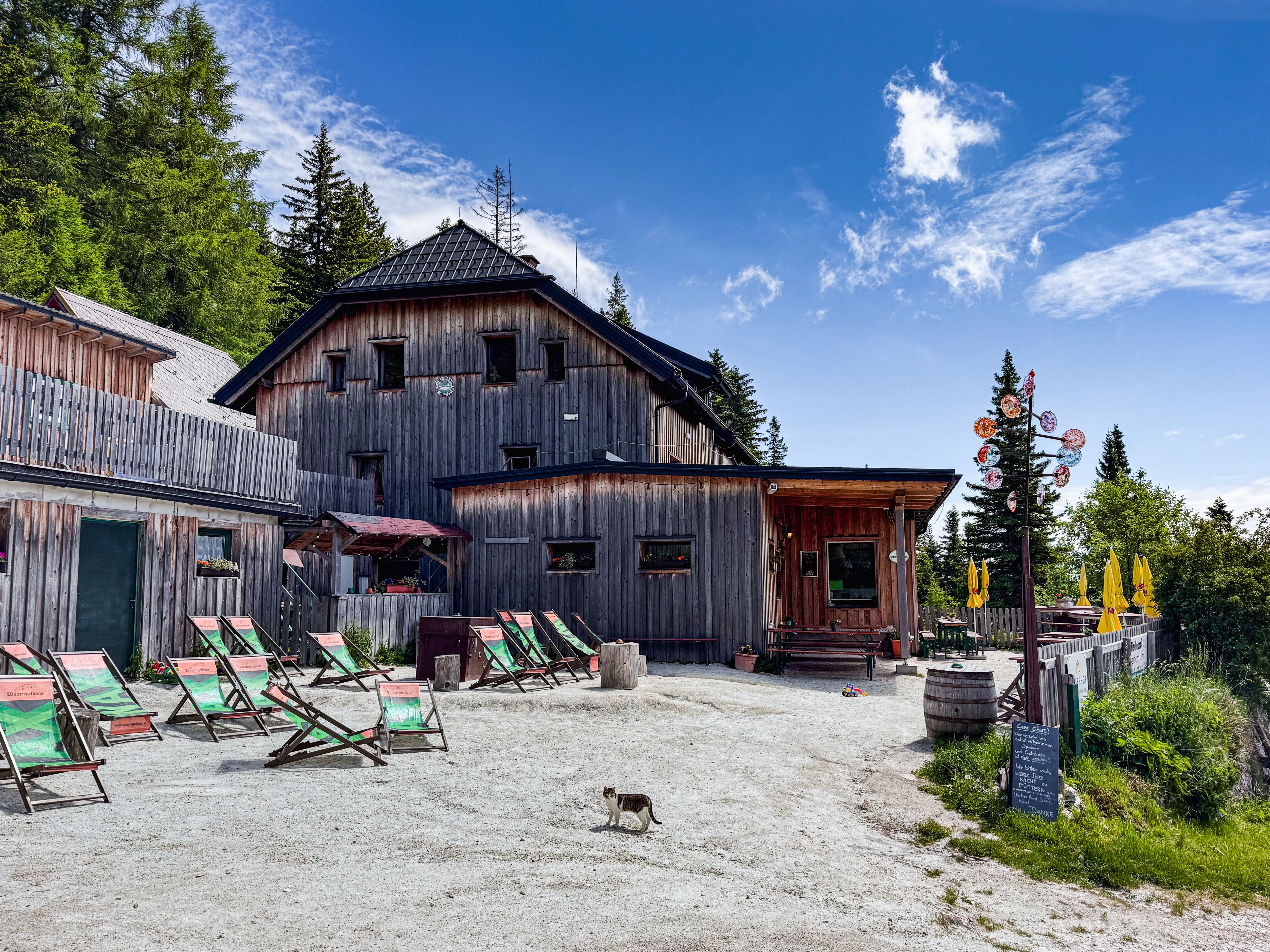 Ein rustikales Holzgebäude in einer Berglandschaft mit Liegestühlen und Sonnenschirmen im Vordergrund.