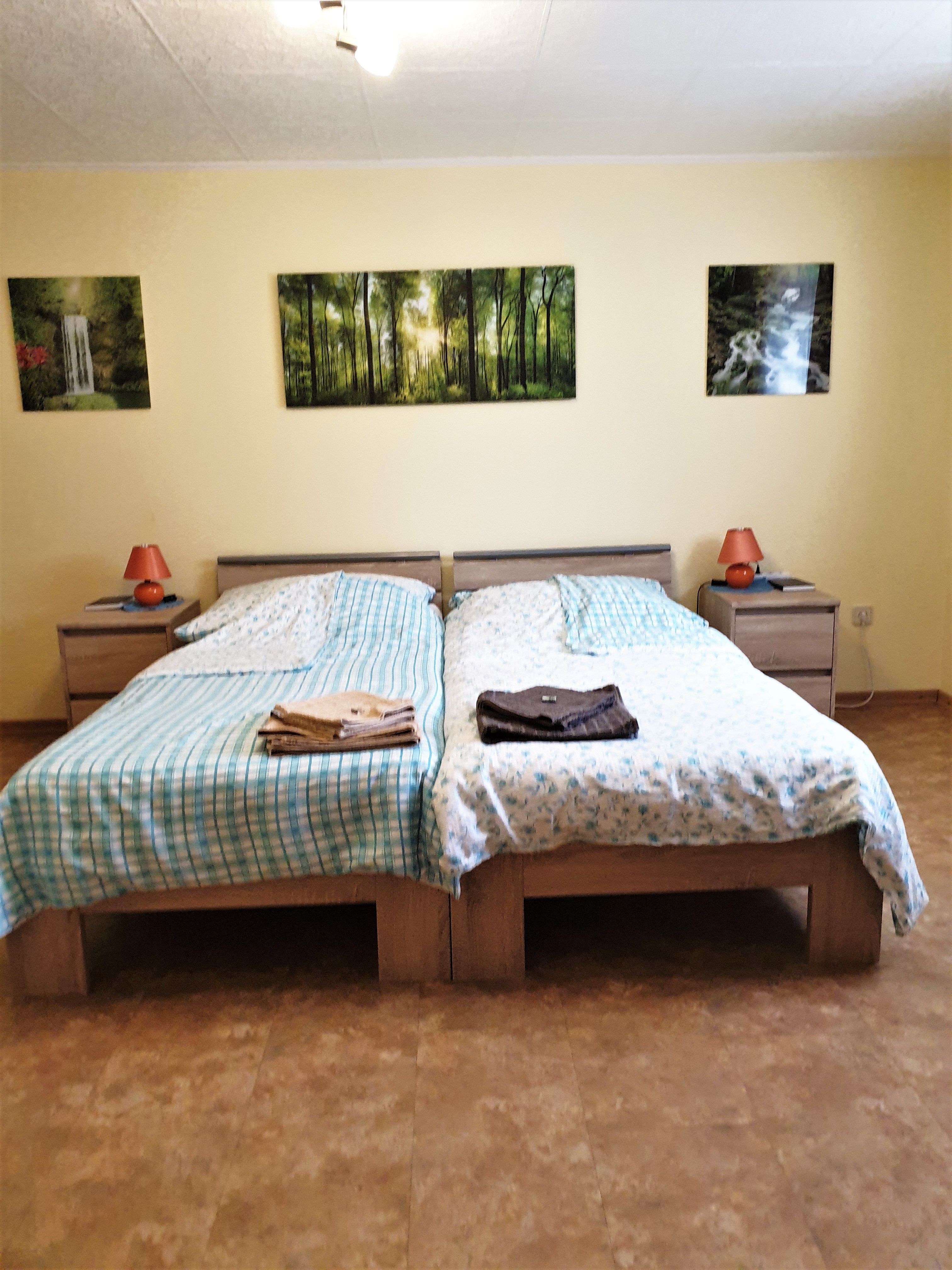 Schlafzimmer mit zwei Einzelbetten, Nachttischen und Waldlandschaftsbildern an der Wand.