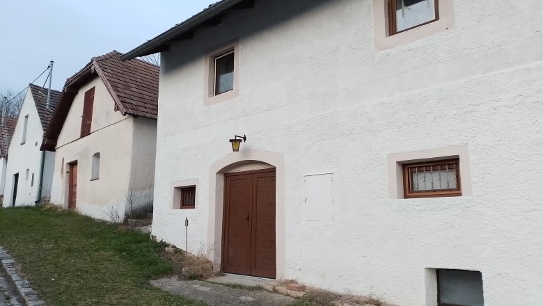 Außenansicht, © Wein-Bleibe Reihen von weißen Häusern mit braunen Türen und Fenstern, entlang einer Straße mit Grasstreifen.