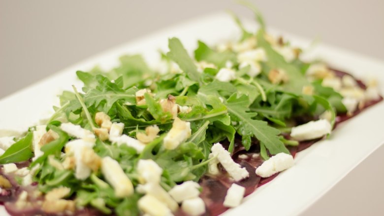 Ein Teller mit Rucola, K&auml;se und N&uuml;ssen auf d&uuml;nnen Fleischscheiben.