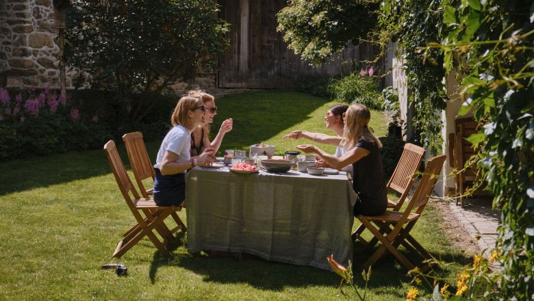 Vier Frauen sitzen an einem Tisch im Garten und genie&szlig;en eine Mahlzeit.