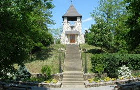 Steinturm auf einem H&uuml;gel mit Treppe und gr&uuml;ner Umgebung.