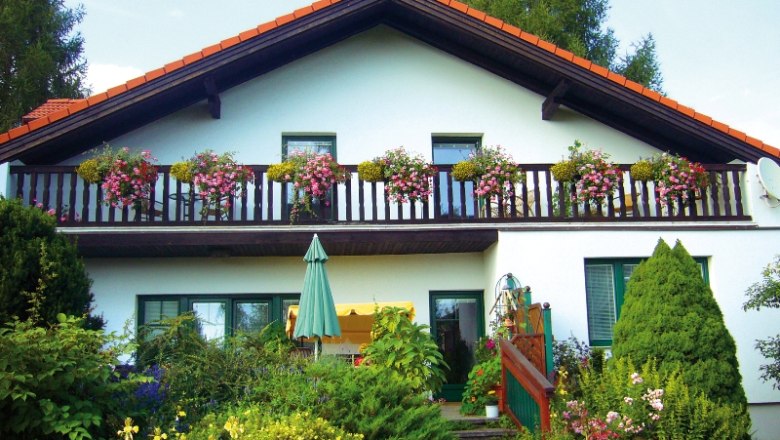 Ein zweist&ouml;ckiges Haus mit Balkon und Blumen.