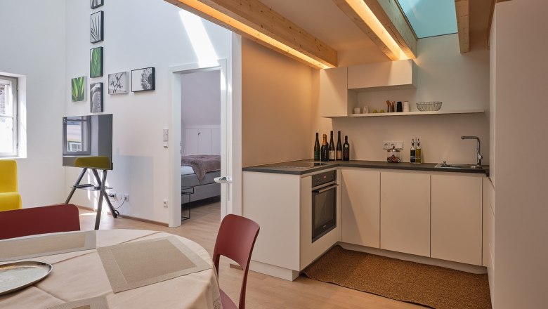 Moderne K&uuml;che mit Holzbalken, Esstisch und Blick ins Schlafzimmer.